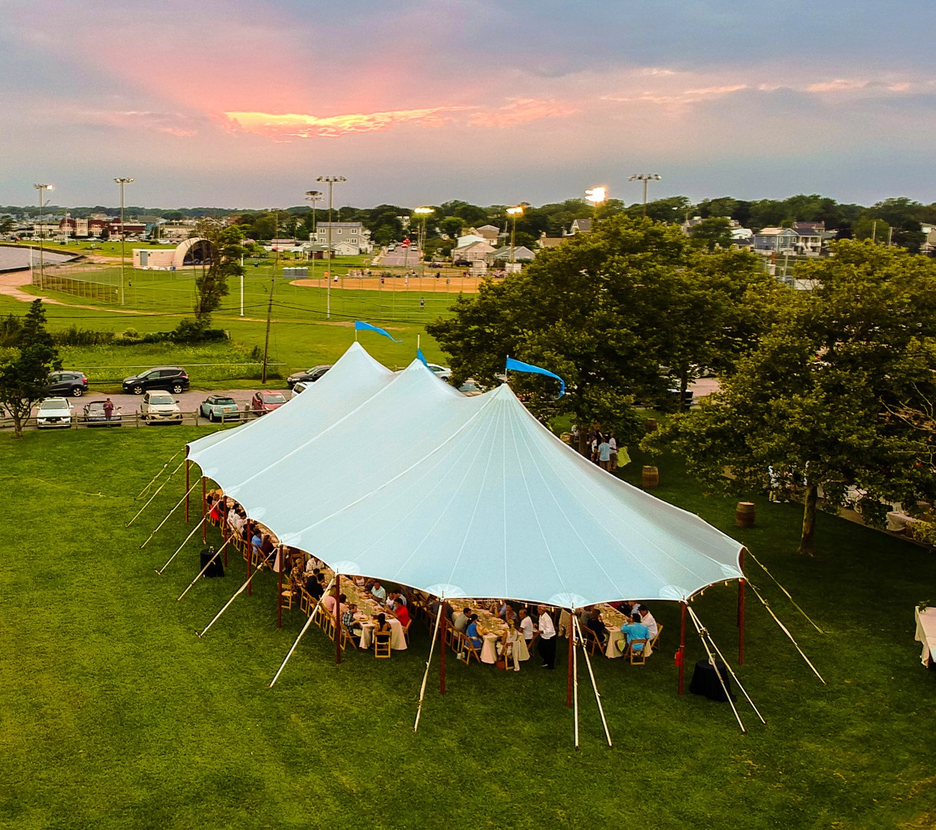 Sailcloth marquee set up on a grassy field with wooden poles, photographed from above during an outdoor evening event.